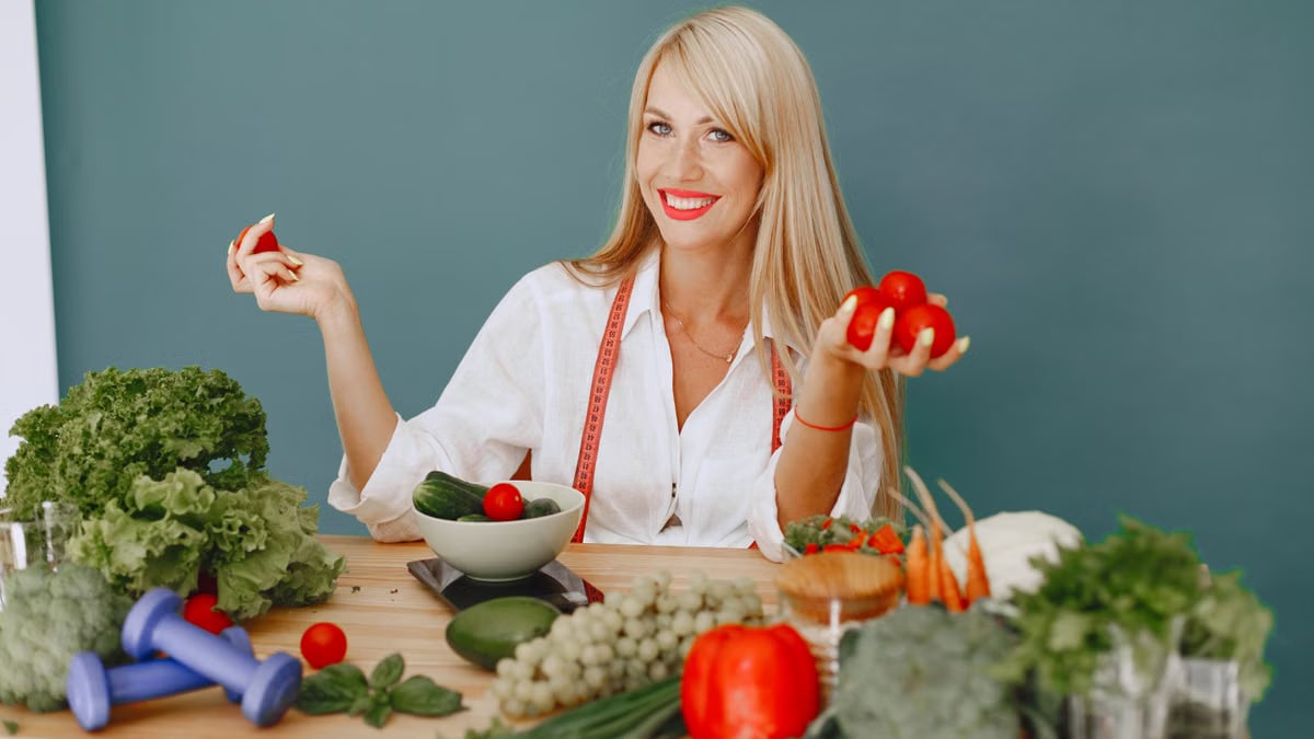 Healthy lifestyle concept with woman holding tomatoes and surrounded by fresh vegetables in a studio setting.