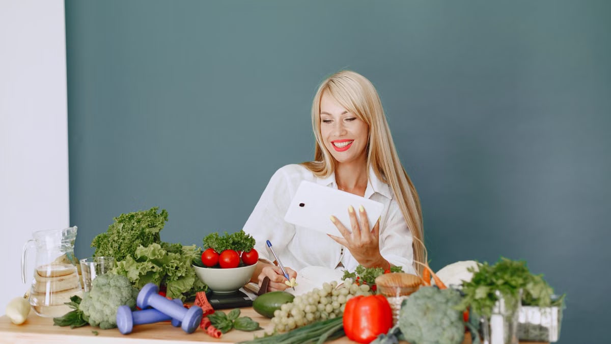 Woman using a tablet surrounded by fresh vegetables at a table, showcasing healthy lifestyle and technology.